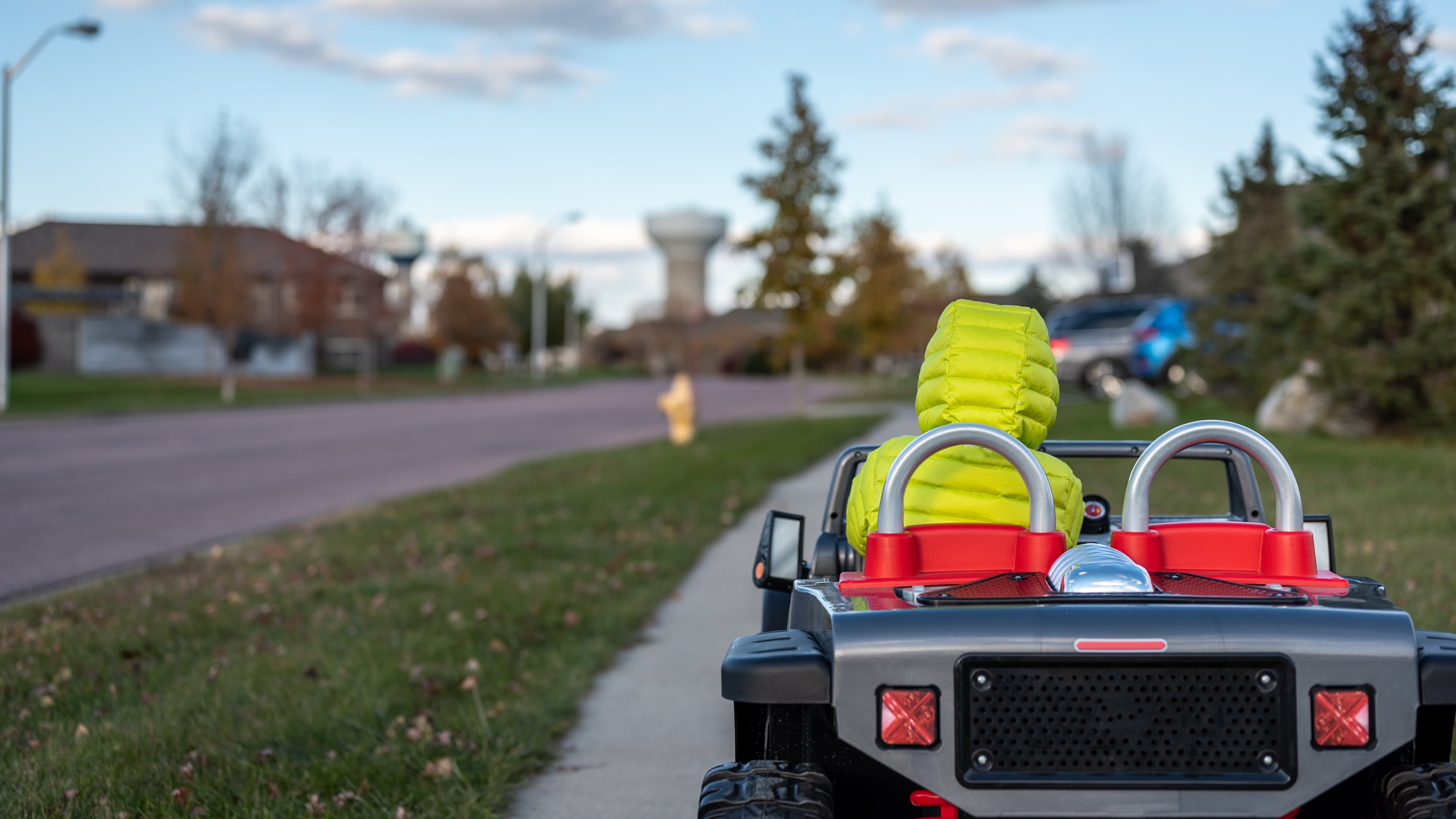boy driving an electric toy car down a sidewalk.