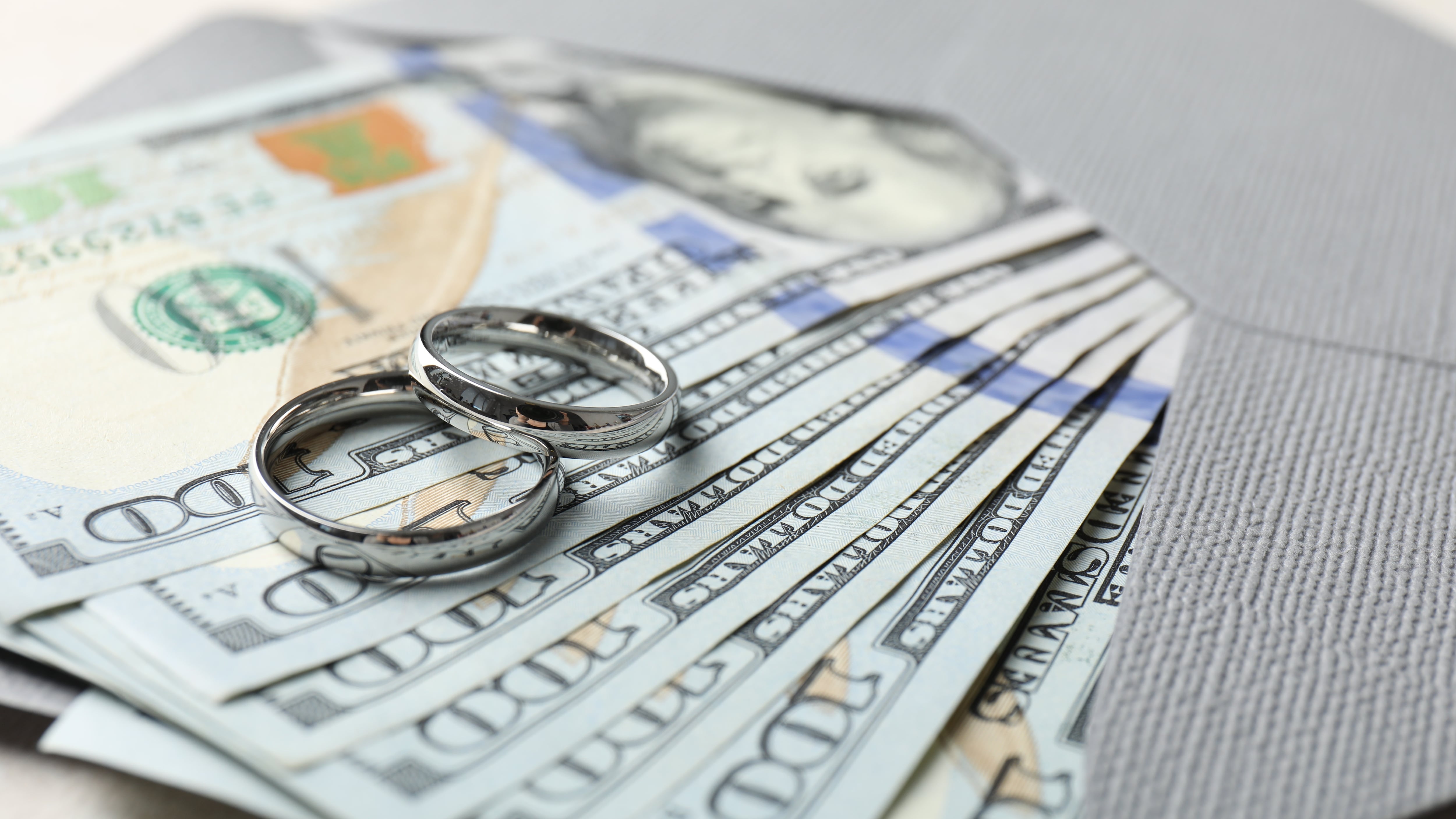 Two silver wedding rings, dollar banknotes and envelope on white table, closeup
