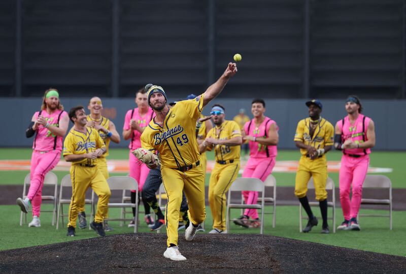 NEW YORK, NEW YORK - AUGUST 12:  Ryan Kellogg #49 of the Savannah Bananas warms up between innings as his team performs a dance routine behind him during their game against the Party Animals at Richmond County Bank Ball Park on August 12, 2023 in New York City.  The Savannah Bananas were part of the Coastal Plain League, a summer collegiate league, for seven seasons. In 2022, the Bananas announced that they were leaving the Coastal Plain League to play Banana Ball year-round. Banana Ball was born out of the idea of making baseball more fast-paced, entertaining, and fun.   (Photo by Al Bello/Getty Images)